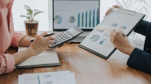 デスクの上でグラフや計算機を使いながら資料を確認している二人のビジネスパーソン。