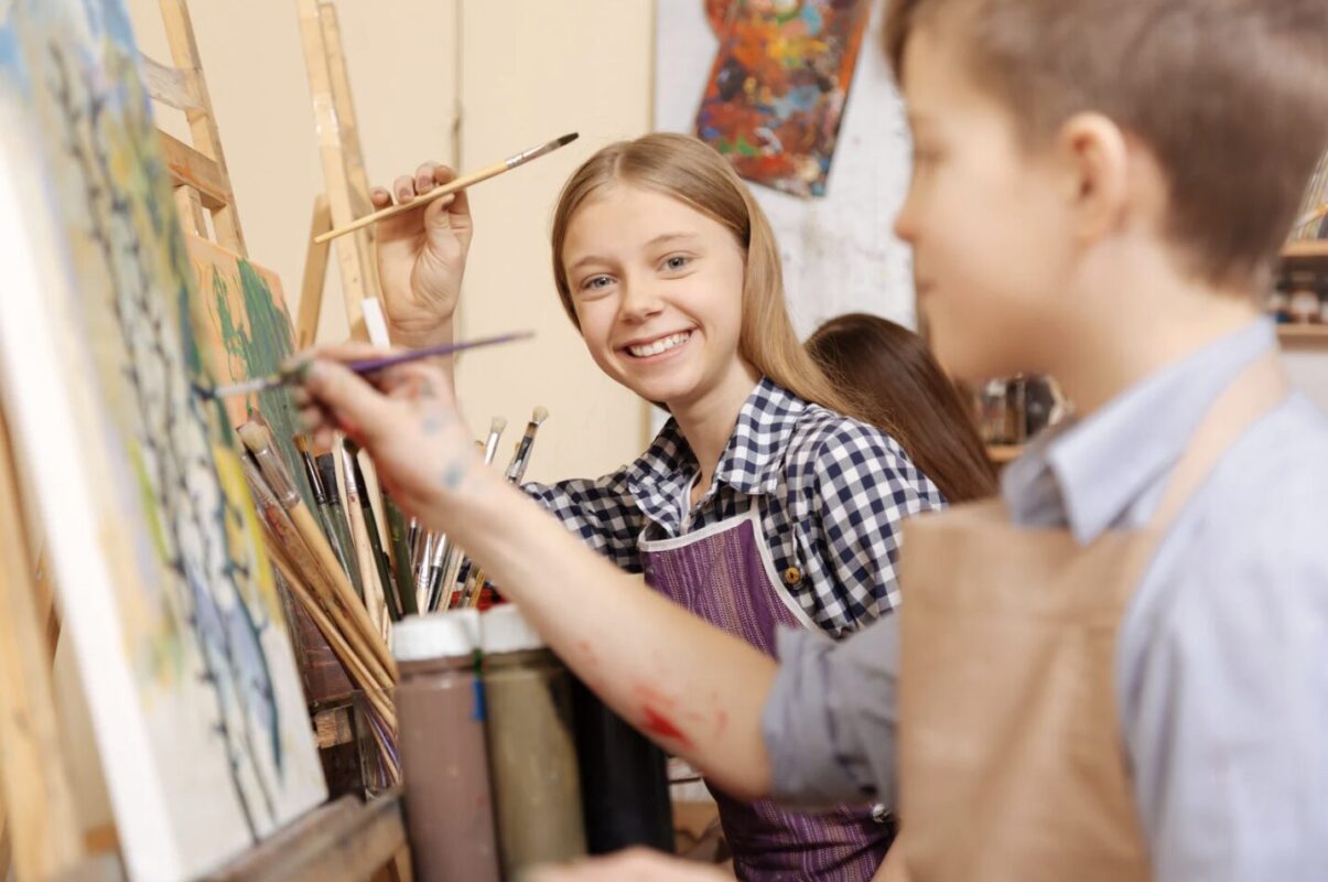 アートクラスで笑顔を見せながらキャンバスに絵を描く子どもたち、創作を楽しむ様子。
